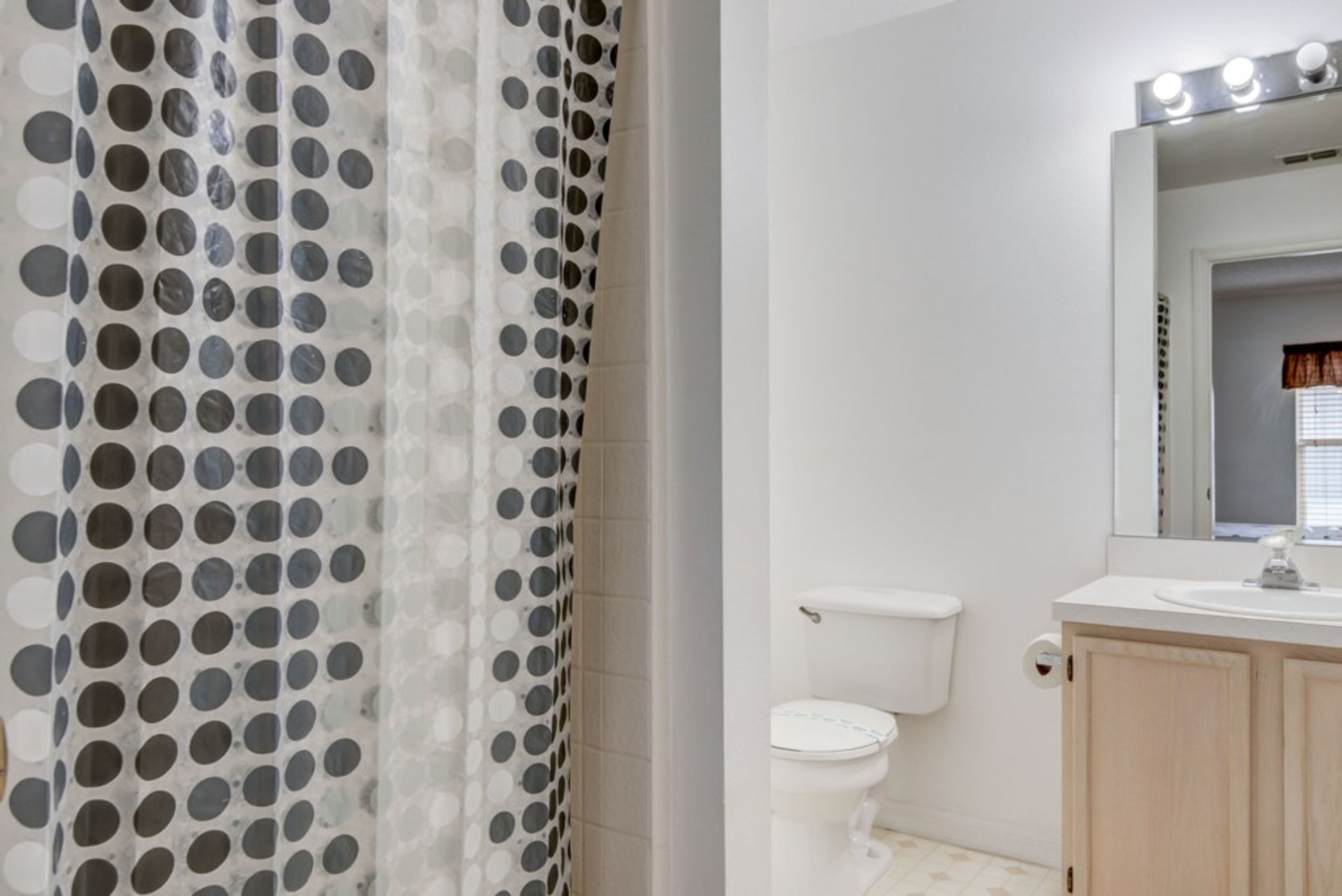 A bathroom with a toilet, a sink, and a mirror with lights.