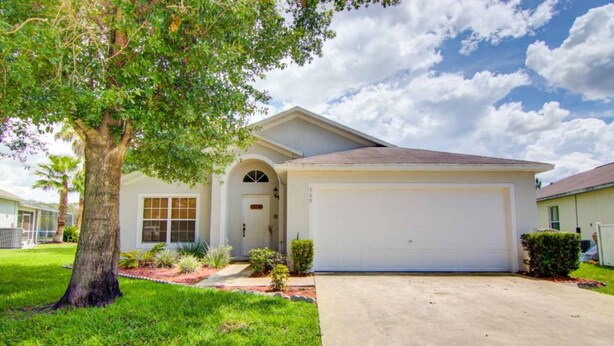 A single-story house with a garage, a well-maintained lawn, and a tree in the front yard. - Clear Creek 909 (Clermont)
