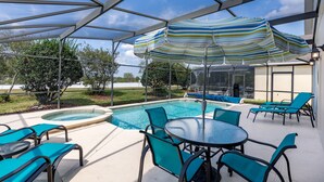 Un espace extérieur abrité comprenant une piscine, des chaises longues et une table placée sous un parasol à rayures.