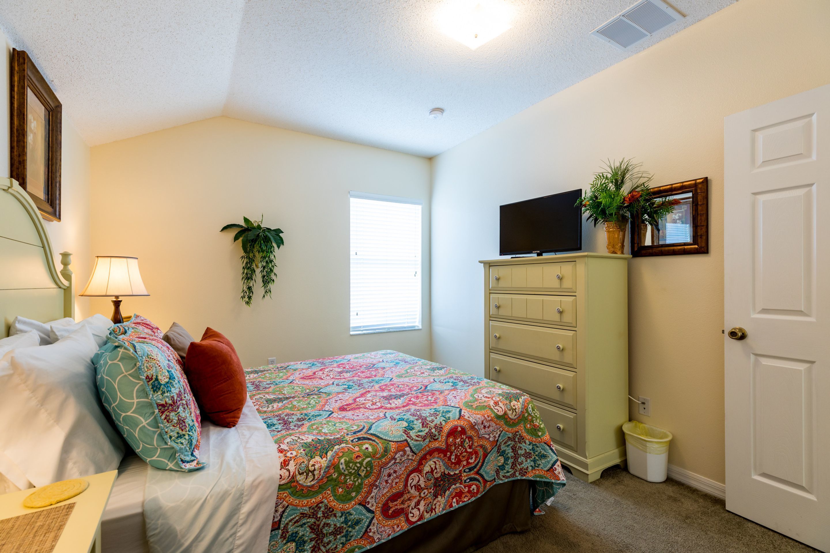 A bedroom with a bed, dresser, television, and a window.