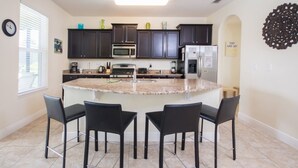 Una cocina moderna con armarios oscuros, una isla central con taburetes de bar, microondas, horno y refrigerador.