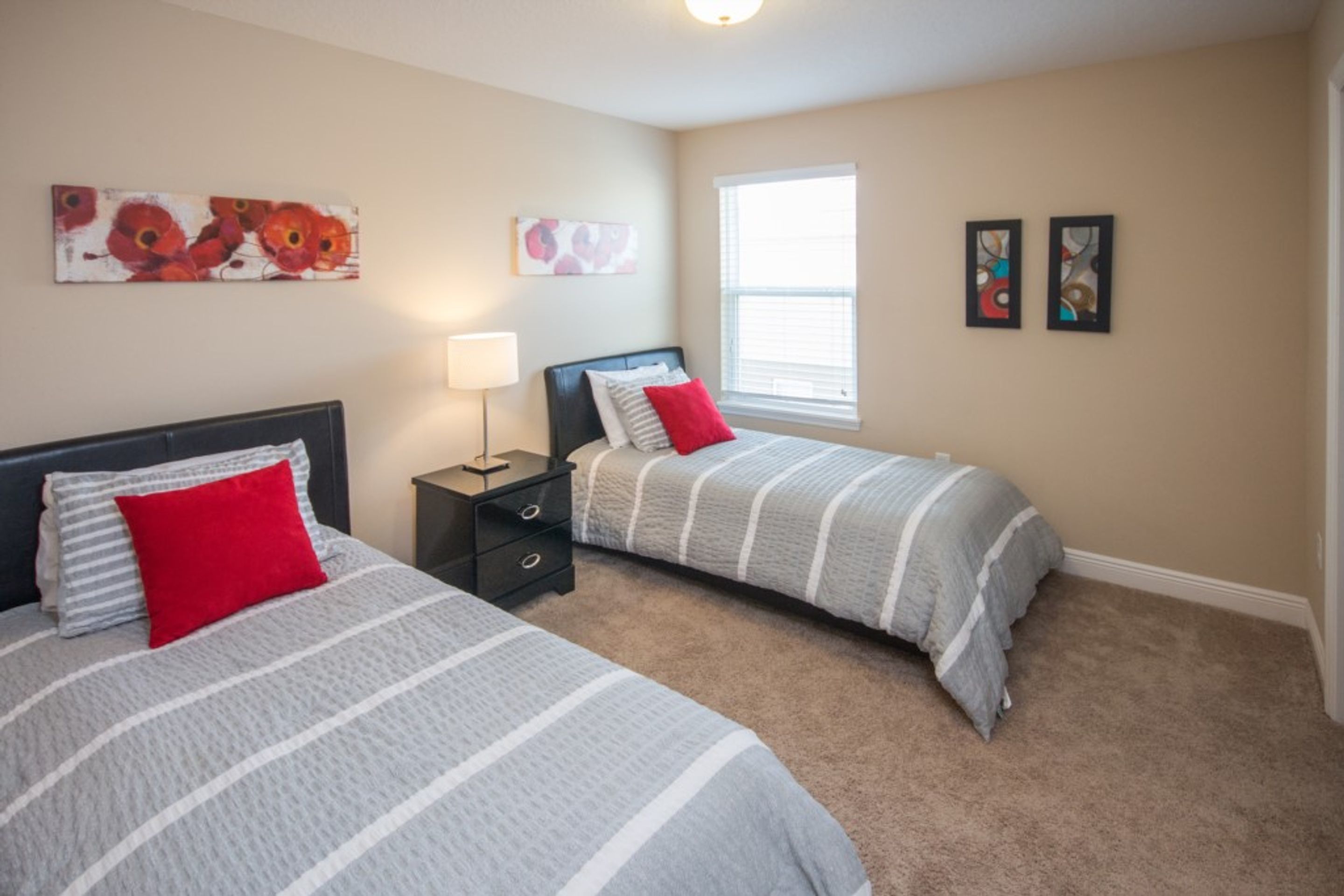 A bedroom with two beds, a nightstand, a lamp, and artwork on the walls.