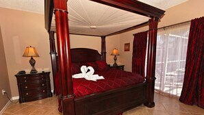 Uma cama de dossel com colcha vermelha, duas mesas de cabeceira com luminárias e uma janela com cortinas.