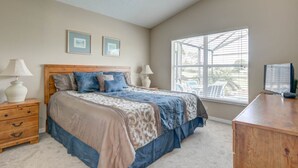 Quarto com uma cama grande, duas mesas de cabeceira, cômoda e uma janela com persianas.