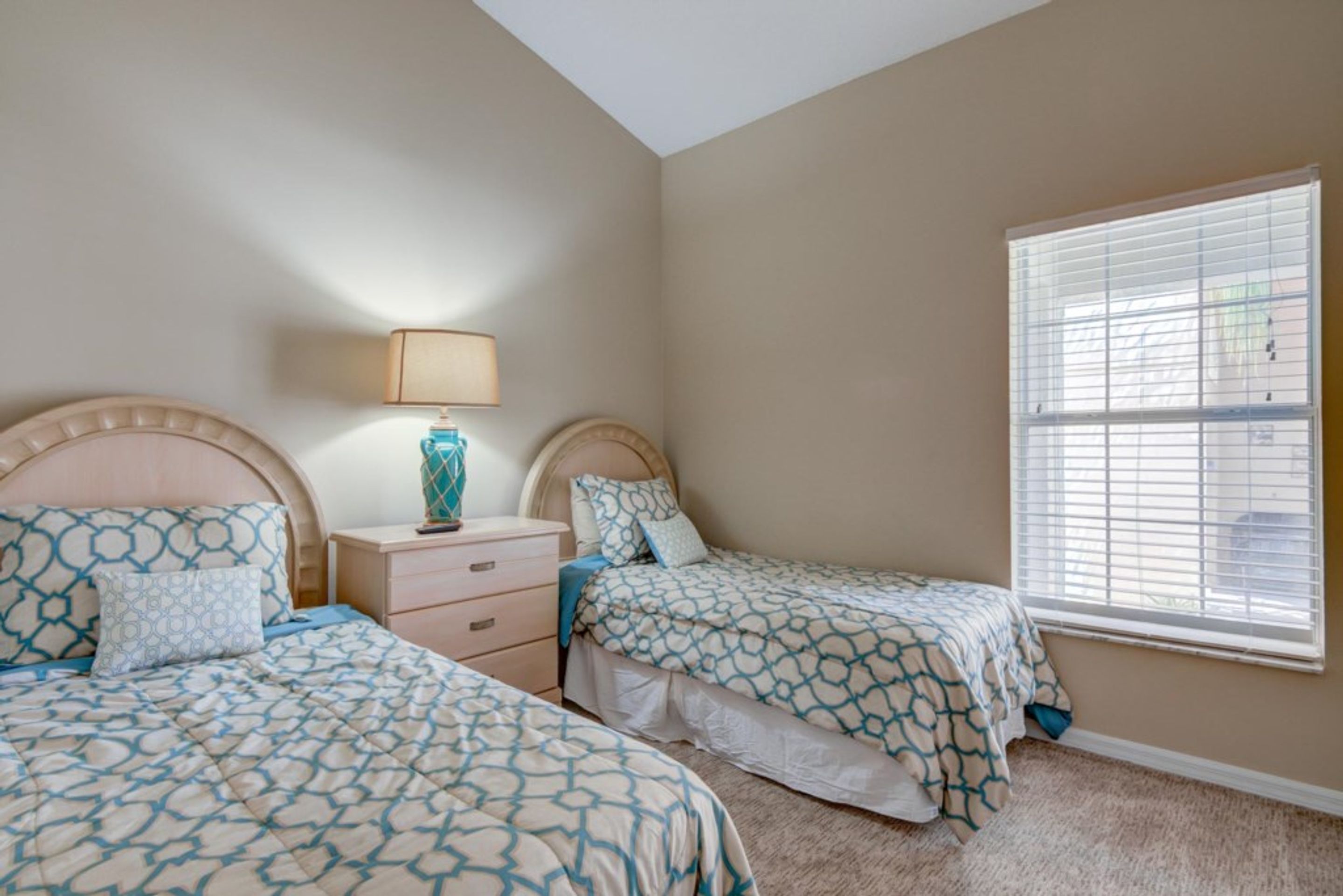 A bedroom with two beds, a nightstand, a lamp, and a window with blinds.