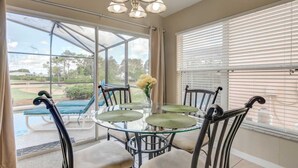 Uma sala de jantar com mesa e cadeiras de vidro, um candelabro e vista para um campo de golfe através de grandes janelas.