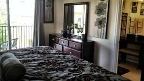 A bedroom with a bed, dresser, and a large mirror. There is a balcony with a chair and curtains.
