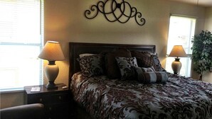 A bedroom with a large bed, two bedside tables with lamps, a decorative wall piece, and a potted plant.
