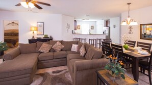 A living room with a sectional sofa, a dining table with chairs, a ceiling fan, and a kitchen in the background. - Cypress Pointe 1097 (Davenport)