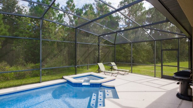 A swimming pool with a glass enclosure, surrounded by lounge chairs and a view of a forested area. - Cypress Pointe 1097 (Davenport)