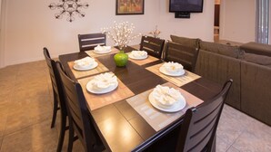 A dining area with a table set for six, surrounded by chairs, a green vase with branches, and a chandelier on the wall. - Cypress Pointe 1097 (Davenport)