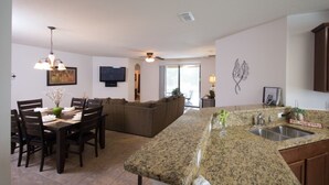 A spacious kitchen with granite countertops, a dining area with wooden chairs, and a living room with a sofa. - Cypress Pointe 1097 (Davenport)