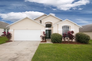 A single-story house with a garage, a front entrance, and a small front yard with shrubs and a lawn. - Rolling Hills 7930 (Kissimmee)