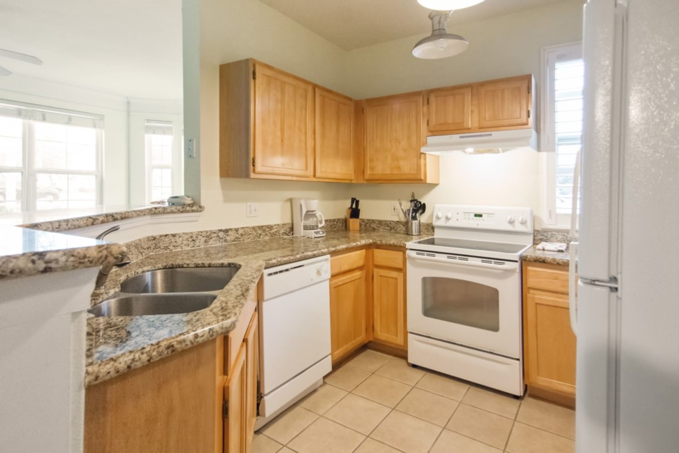 A kitchen with granite countertops, wooden cabinets, a white dishwasher, an oven, and a refrigerator.