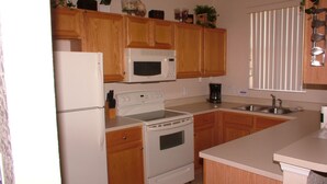A kitchen with wooden cabinets, a white refrigerator, a microwave, a stove, and a sink. - Regal Palms Resort & Spa 124 (Davenport)