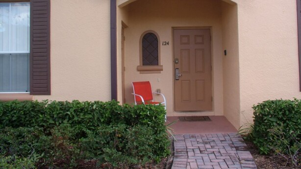 A building entrance with a brown door marked "124," a red chair outside, and a brick pathway leading to the door. - Regal Palms Resort & Spa 124 (Davenport)