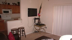 A compact living space with a kitchenette, a flat-screen TV, a small table with a vase, and a leather couch with red cushions. - Regal Palms Resort & Spa 124 (Davenport)