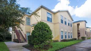 A two-story residential building with a red staircase, a small green bush, and a clear sky. - Club Cortile 2730b (Kissimmee)