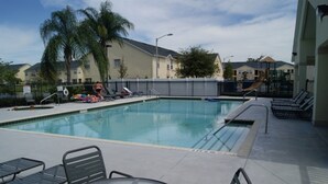 A swimming pool with lounge chairs and a table, surrounded by a fence and palm trees. - Club Cortile 2730b (Kissimmee)