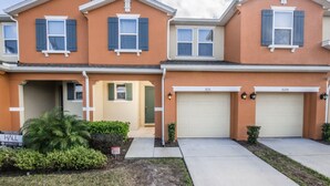 A two-story townhouse with a beige exterior, blue shutters, and a garage with two doors. - Compass Bay 3131 (Kissimmee)