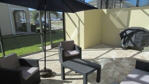 An outdoor patio area with wicker furniture, a large umbrella, and a grill. - Compass Bay 3131 (Kissimmee)