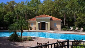 A poolside area with a building, palm trees, and lounge chairs. - Compass Bay 3131 (Kissimmee)
