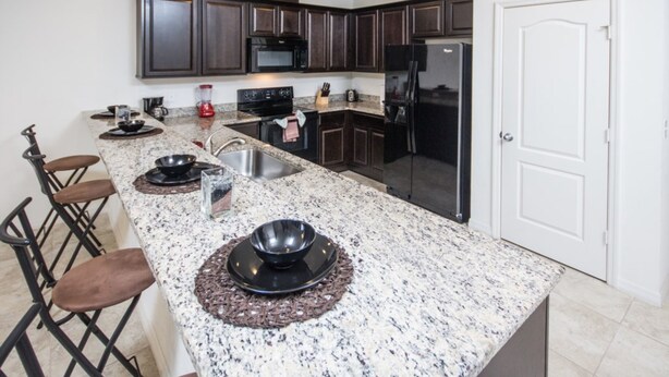 A modern kitchen with dark wood cabinets, stainless steel appliances, and a granite countertop. - Compass Bay 3131 (Kissimmee)