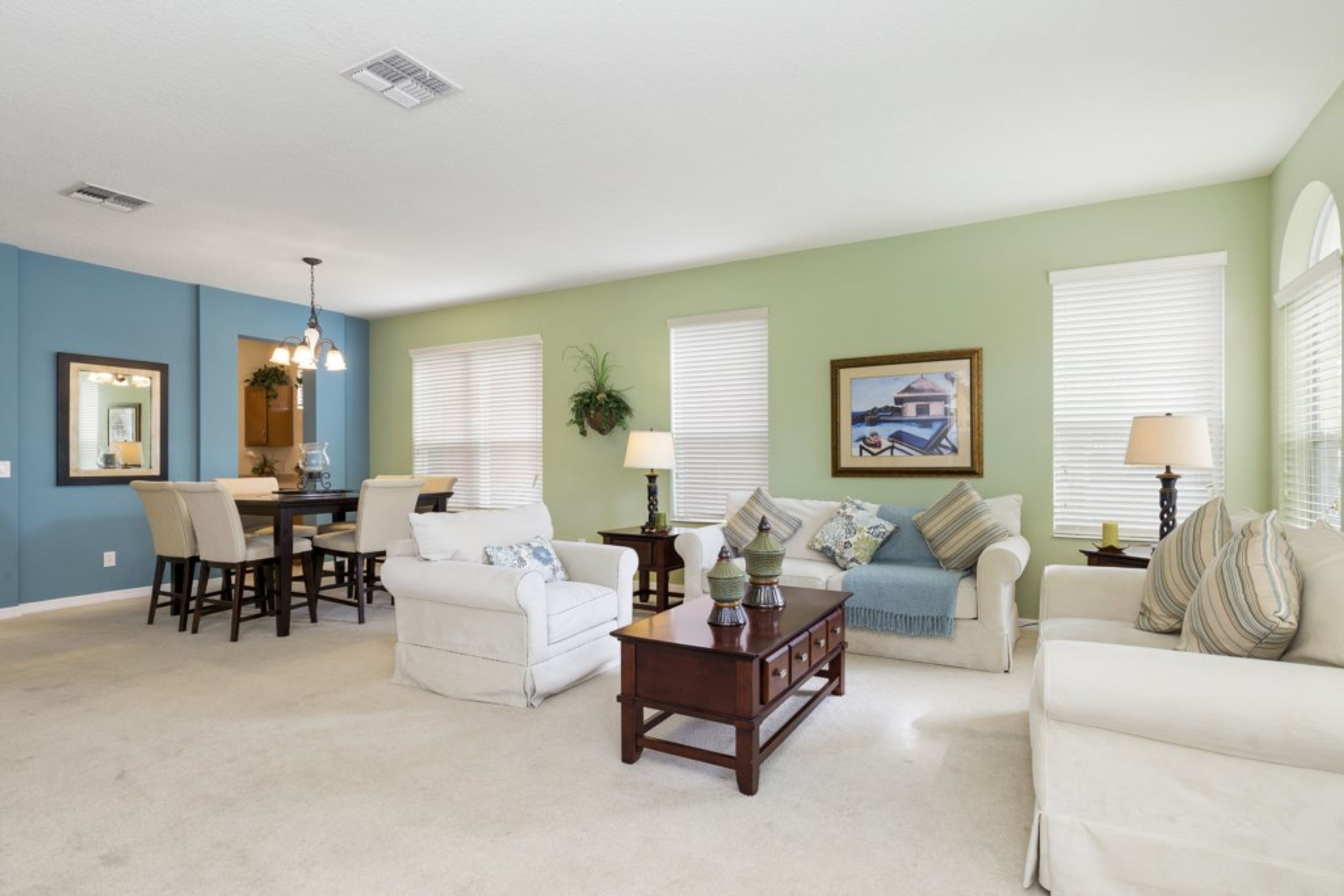 A living room with a dining area, light green walls, white furniture, and a ceiling vent.