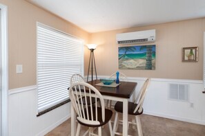 Enjoy meals in this cozy dining area with a table and two chairs, featuring a window with blinds and a framed beach scene.