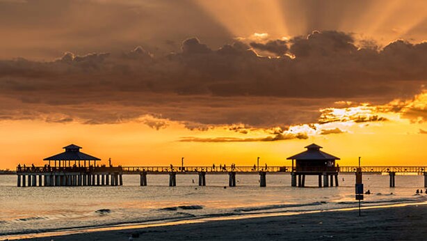 Un muelle que se adentra en el agua, con dos construcciones al final, probablemente miradores, y una puesta de sol al fondo.