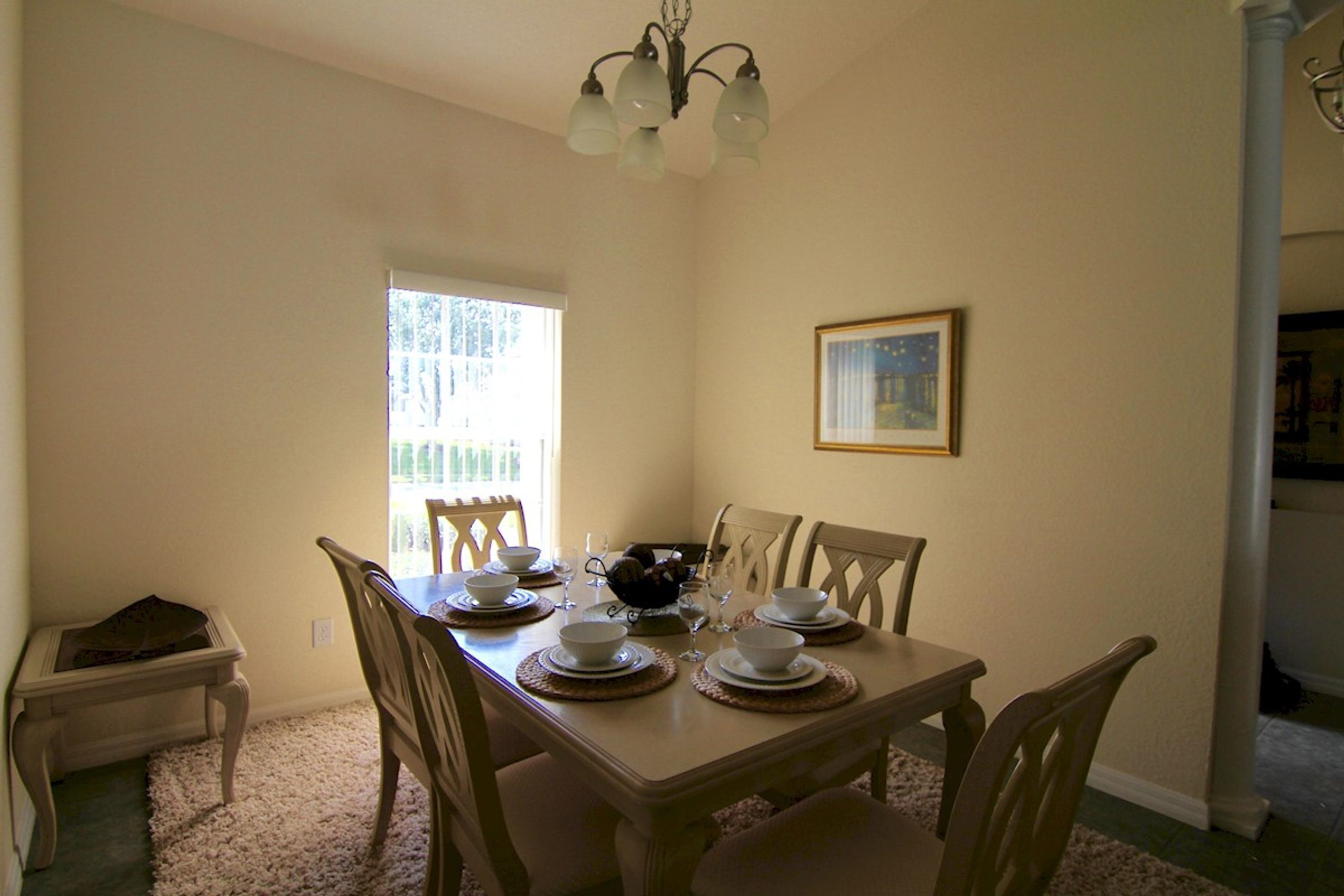 Una sala da pranzo con tavolo imbandito per quattro persone, sedie, un lampadario e una finestra con vista.