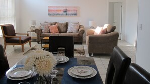 Uma sala de estar com um sofá, uma mesa de jantar posta para dois e um quadro na parede.