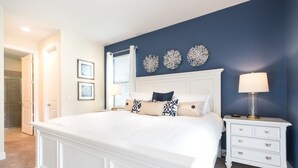 A bedroom with a large bed, white nightstand, and a wall with decorative items. - Encore Resort at Reunion 641 (Kissimmee)