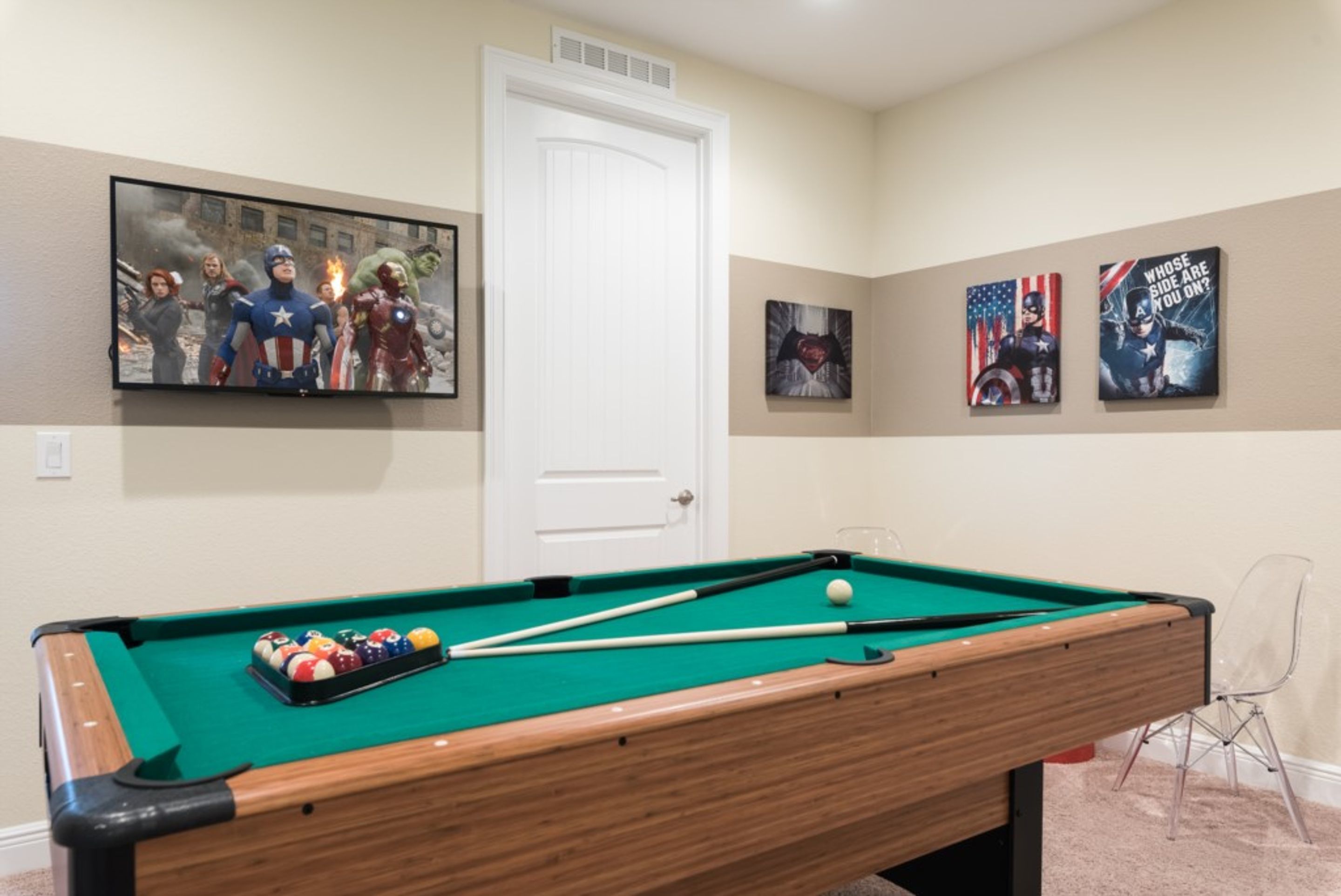 A pool table with pool balls, a television displaying a movie scene, and framed artwork on the wall.