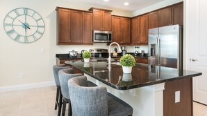 A modern kitchen with wooden cabinets, stainless steel appliances, and a central island with bar stools. - Encore Resort at Reunion 641 (Kissimmee)