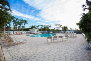 A pool area with lounge chairs and a small building, surrounded by palm trees and a clear sky. - Bonita Beach 5500 - 2806 (Bonita Springs)