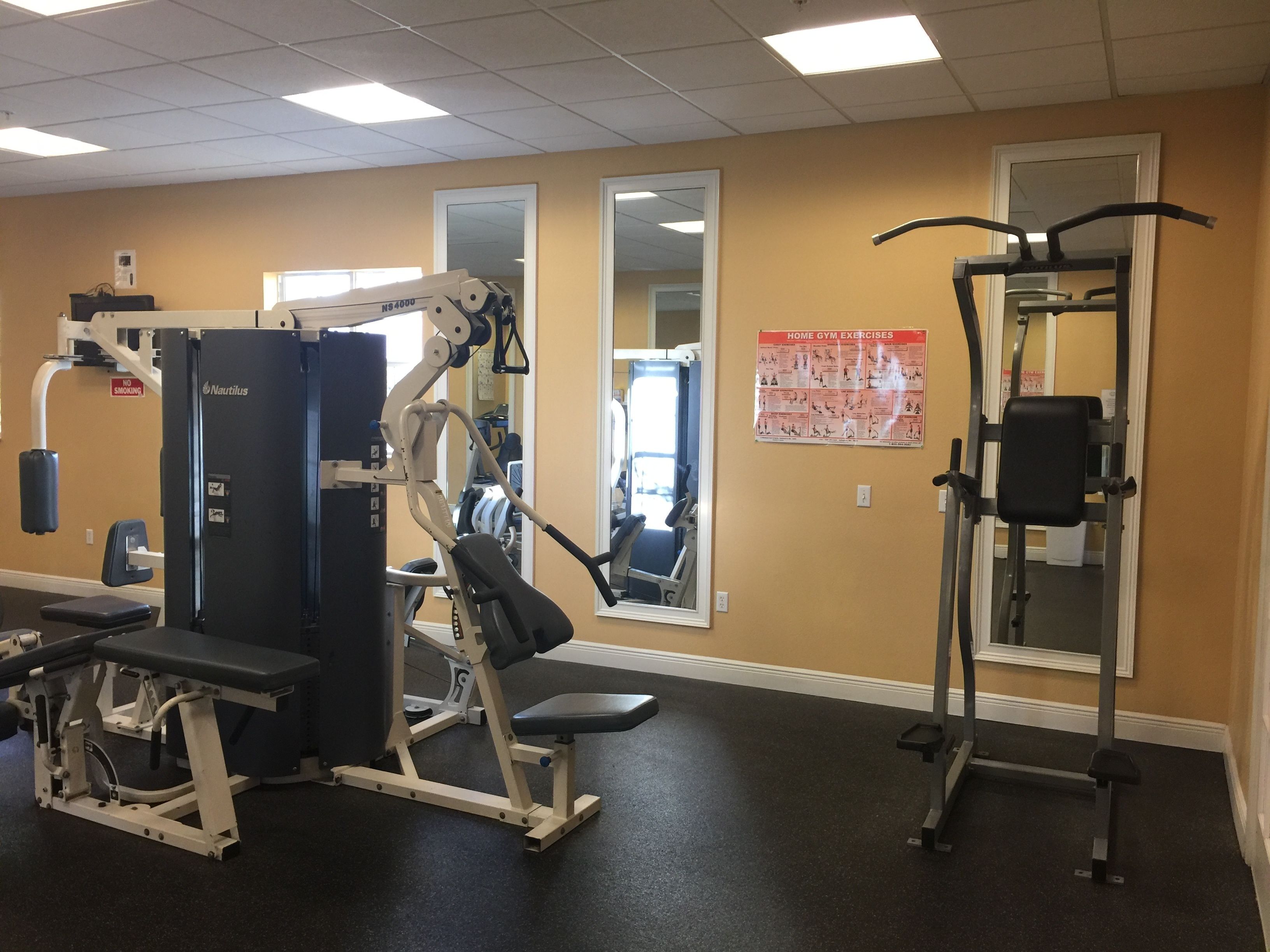 Une salle de sport équipée d'appareils Nautilus, d'un banc de développé couché et d'une barre de traction.