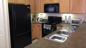 Una cocina con gabinetes de madera, un refrigerador negro, un microondas, una estufa, un lavamanos y un tostador.