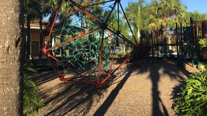 Un parque infantil con una estructura de escalada y palmeras.