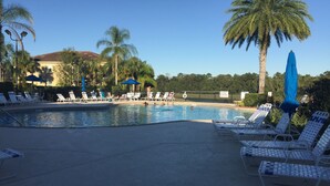Una piscina con sillas de descanso y sombrillas, rodeada de palmeras y una valla.