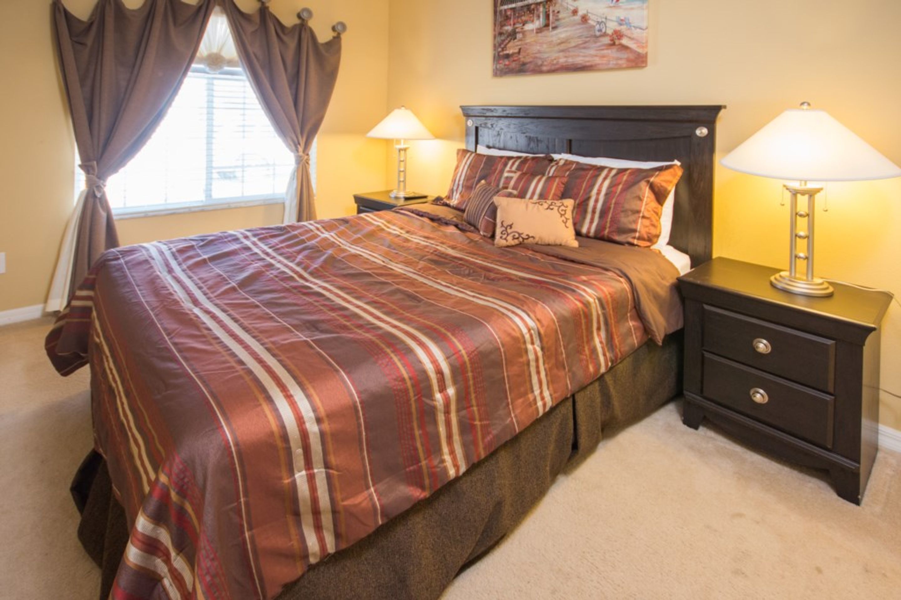 A neatly made bed with a striped bedspread, two bedside tables with lamps, and a window with curtains.