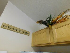 A kitchen with wooden cabinets, a decorative plant, and a motivational sign on the wall. - Highlands Reserve Golf & Country Club 717 (Davenport)