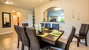 A dining area with a large table, chairs, and a chandelier. There is a kitchen visible in the background. - Cypress Pointe 1132 (Davenport)