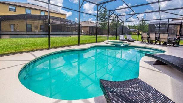 A swimming pool with a glass enclosure, surrounded by lounge chairs and a grassy area. - Cypress Pointe 1132 (Davenport)