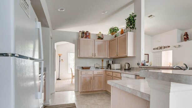 A modern kitchen with light wood cabinets, a built-in oven, and a large island with a sink. - Southern Dunes 2224 (Haines City)