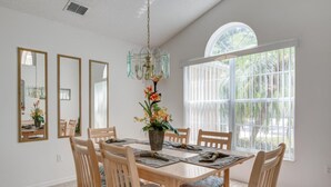 A dining room with a large table, six chairs, a chandelier, and a large window with a view of greenery. - Southern Dunes 2224 (Haines City)
