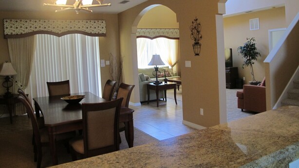 A dining area with a table and chairs, a chandelier, and a view into a living room with a sofa and lamp. - Crystal Cove 4730 (Kissimmee)