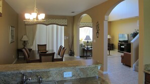 A kitchen with granite countertops, a dining area with a table and chairs, and a living room with a sofa and television. - Crystal Cove 4730 (Kissimmee)