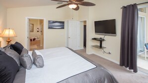 A bedroom with a large bed, a ceiling fan, a TV mounted on the wall, and a door leading to a bathroom. - The Hamlet at Westhaven 320 (Davenport)