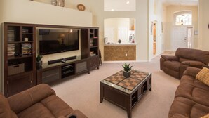 A living room with a large flat-screen TV, brown leather sofas, a coffee table, and a bookshelf. - The Hamlet at Westhaven 320 (Davenport)